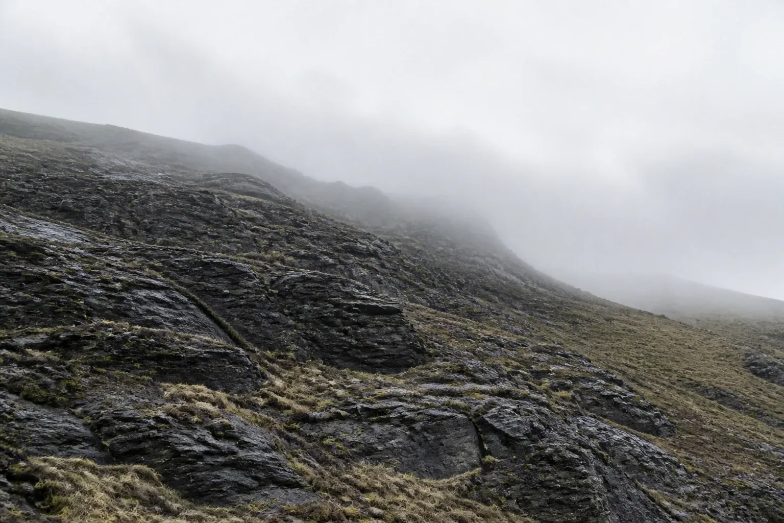 Rain-darkened stone rises diagonally into a bank of pale cloud.