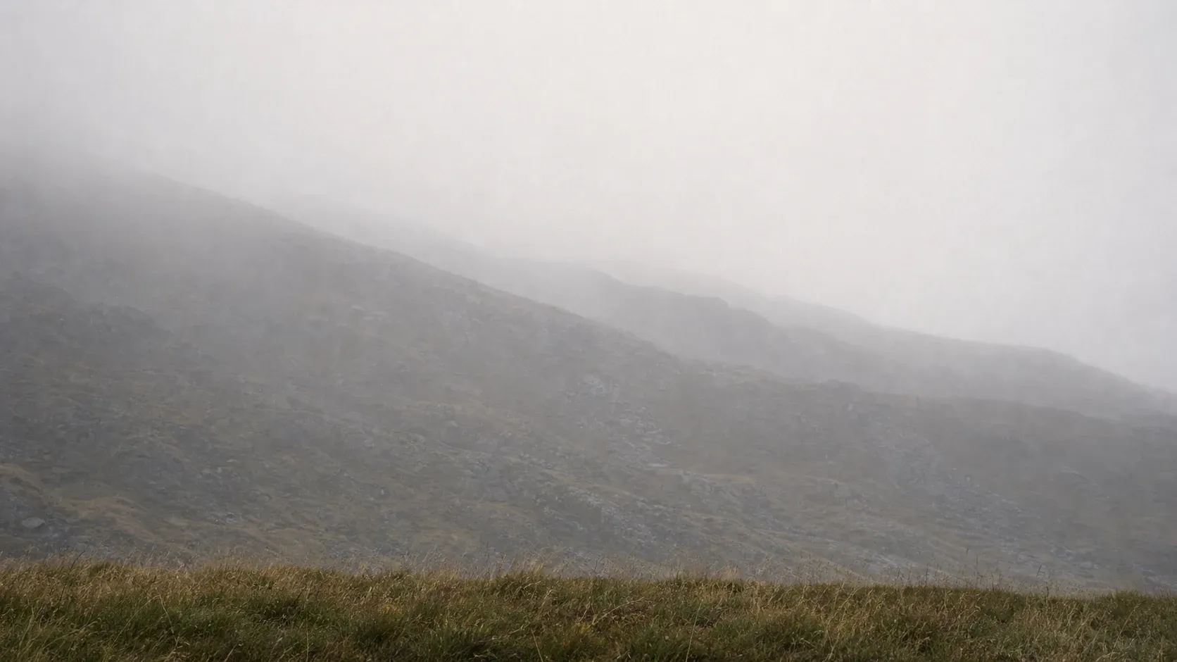 Several gray stone slopes fade into mist above a narrow foreground band of muted grass.